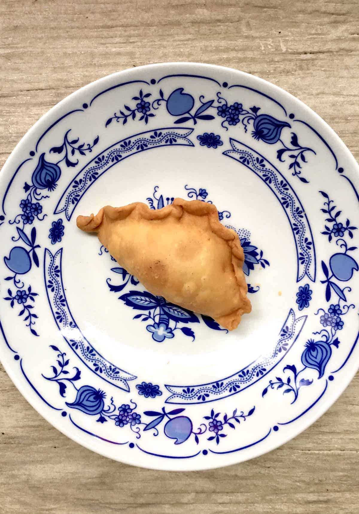 A golden fried vegan curry puff snack on a vintage plate.