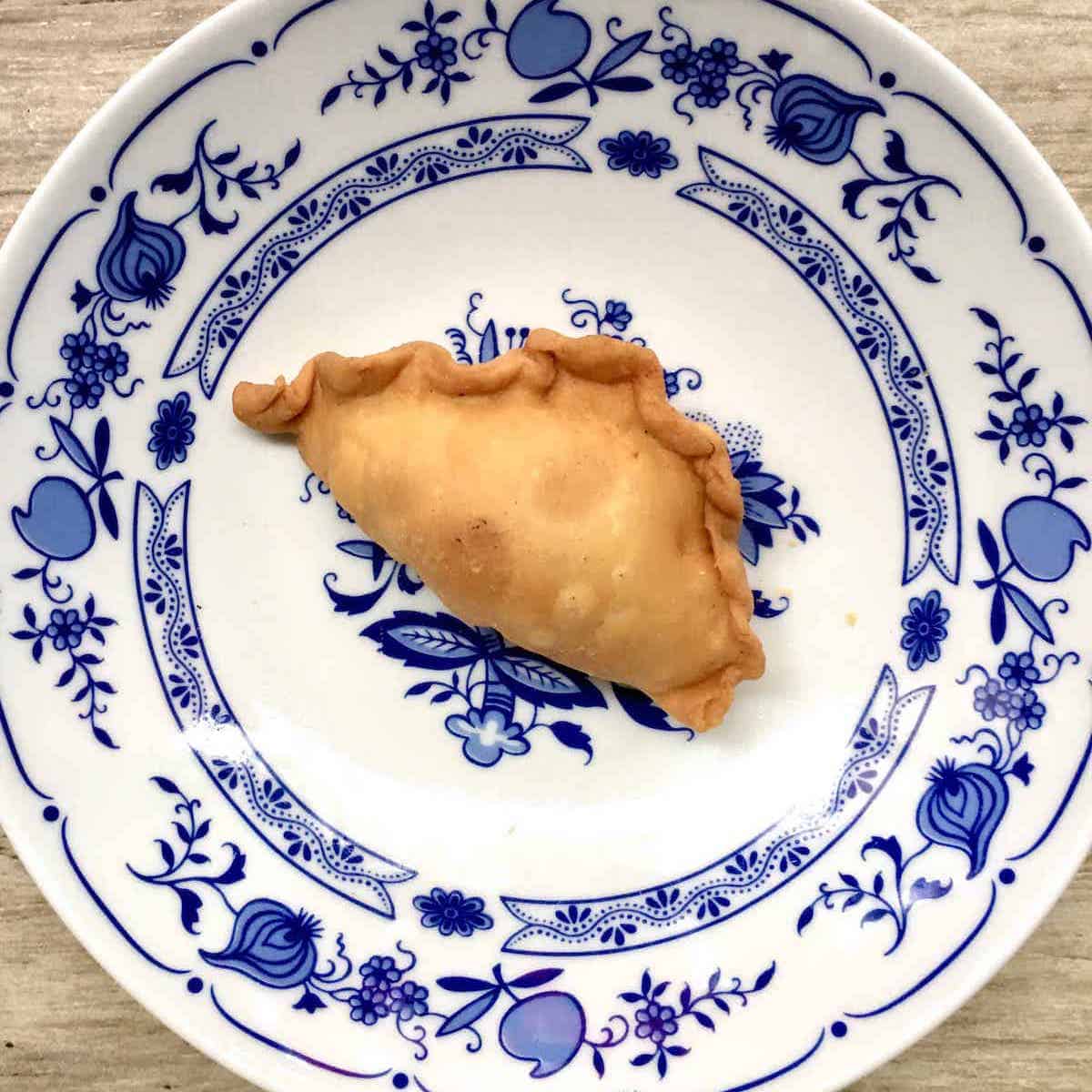 Vegan potato curry puff fried to a crisp golden brown on a plate.