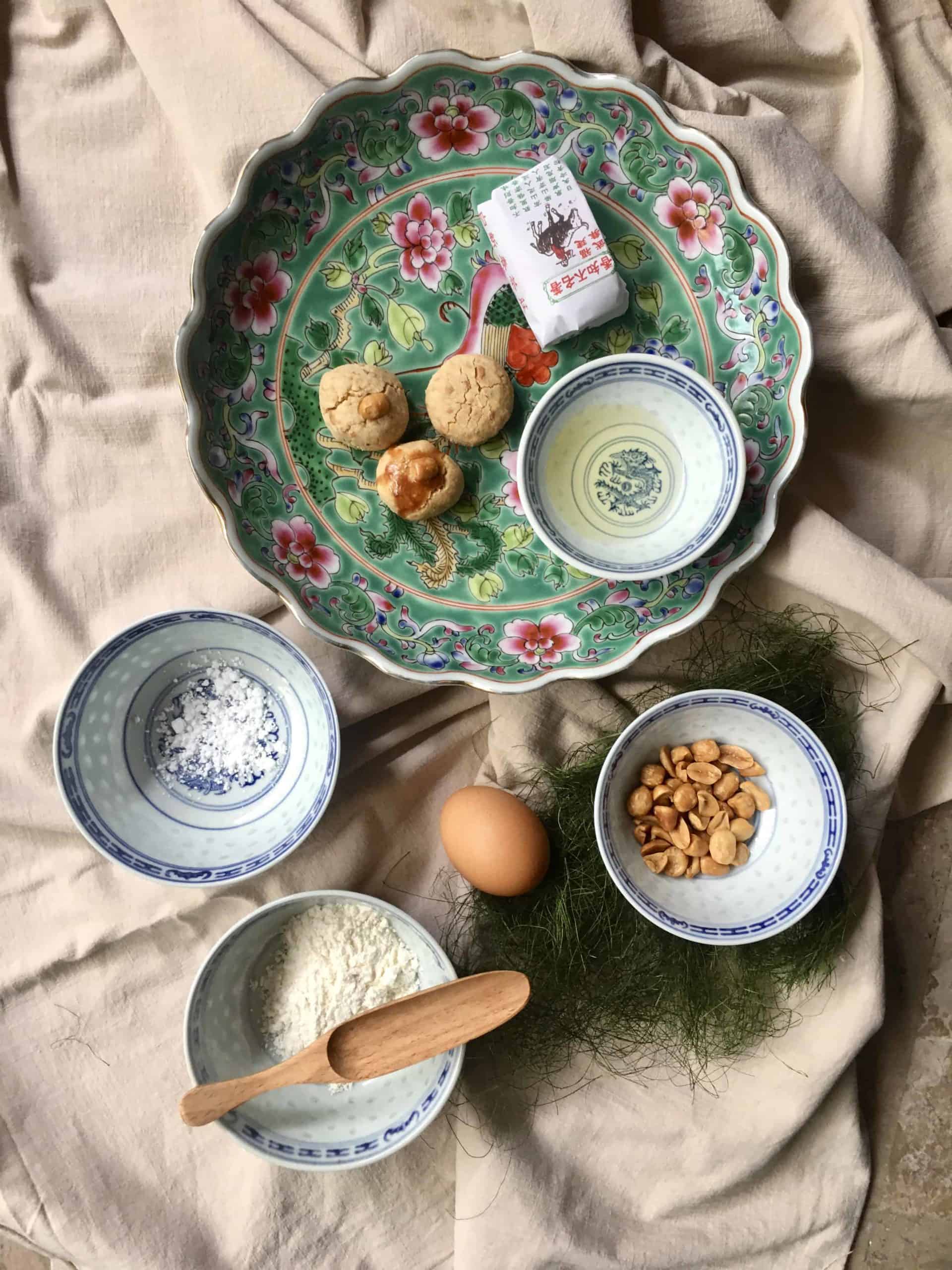 Chinese peanut cookies on a plate with its ingredients peanuts, peanut oil, flour, sugar and egg