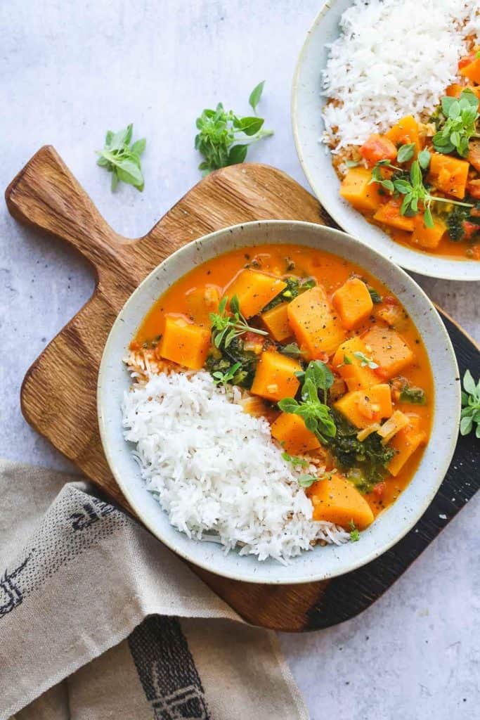 Bowl of lemongrass butternut squash curry with rice and garnished with herbs