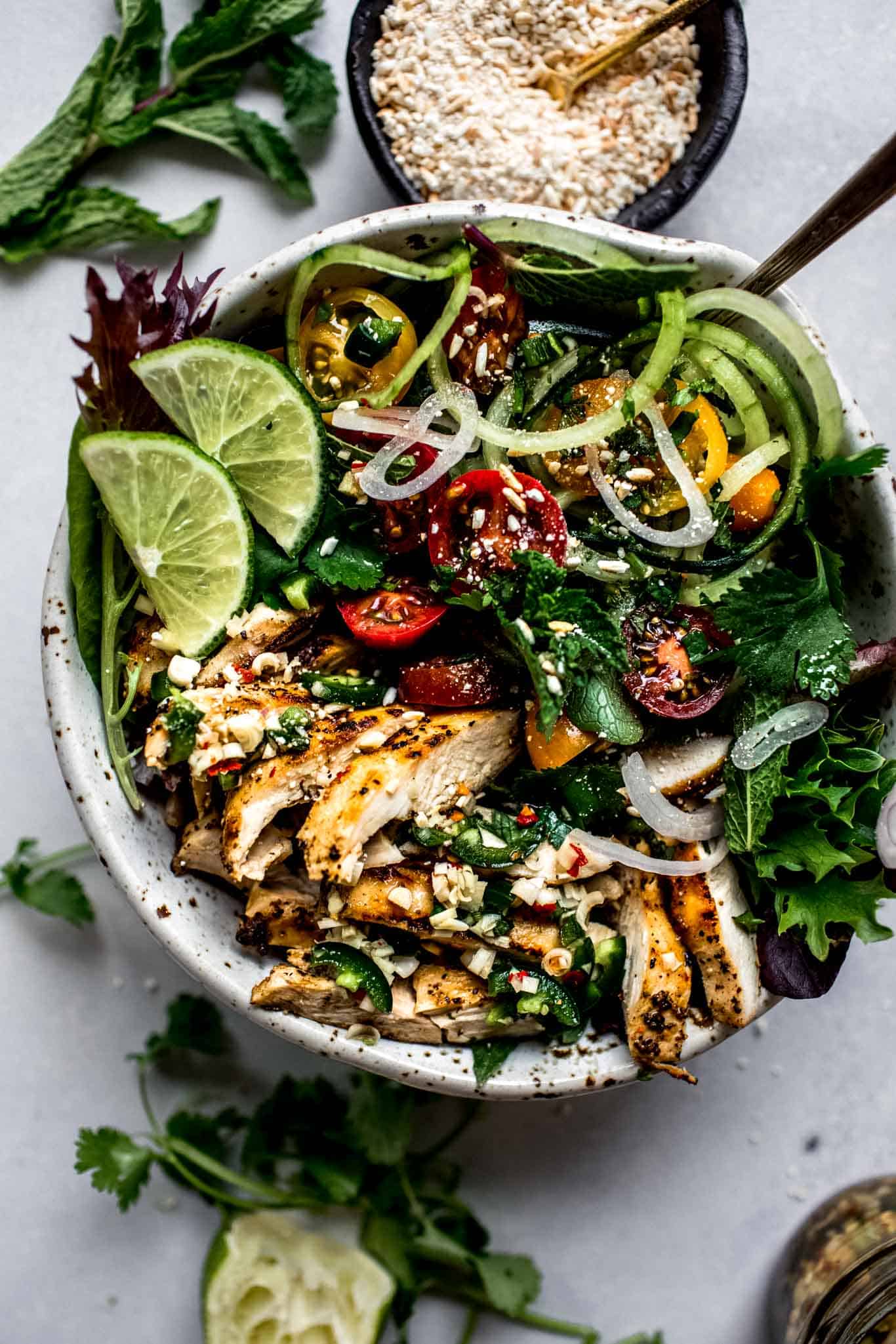 Colourful bowl of Thai chicken salad and greens with slices of lime on the side