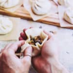 A pair of hands wrapping mushrooms in a vegan bao