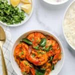A bowl of malabar shrimp curry with a plate of lemons and a bowl of yogurt