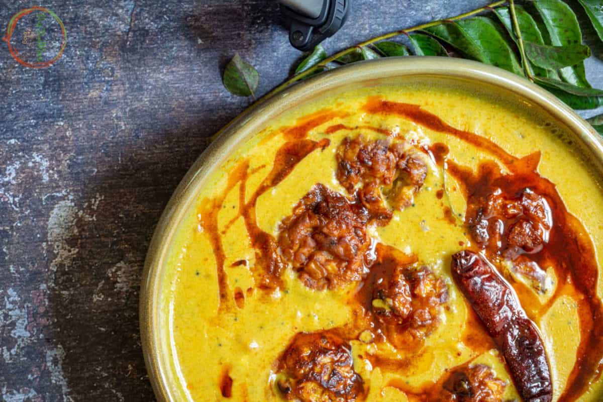 Overhead shot of a bowl of yellow creamy Kadhi with curry leaves.