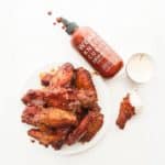 A plate of curry sriracha wings next to a sriracha bottle.