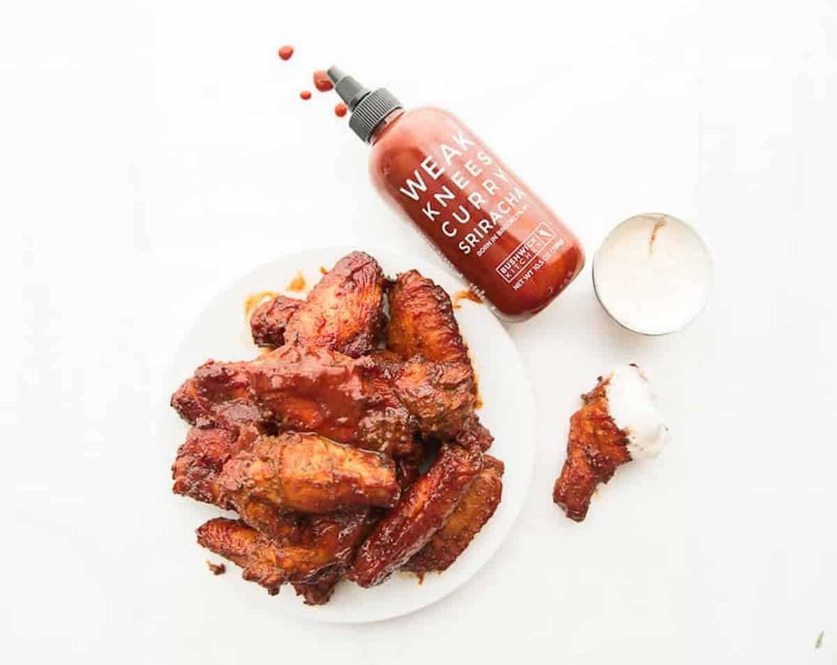 A plate of curry sriracha wings next to a sriracha bottle.