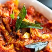 Close-up of red tomato and curry leaf chutney in a white bowl.