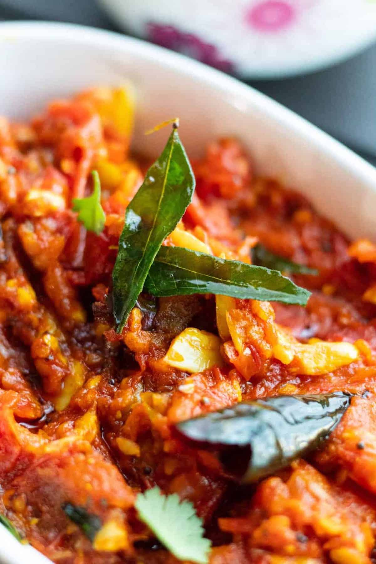 Close-up of red tomato and curry leaf chutney in a white bowl.