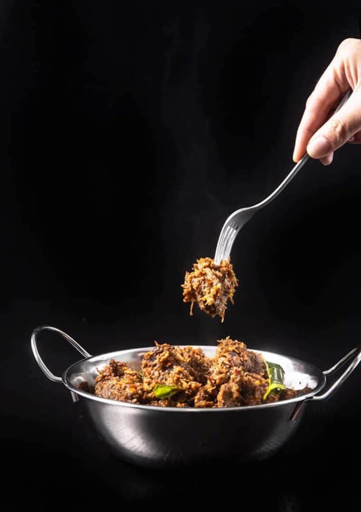 A fork picking up a piece of beef rendang.