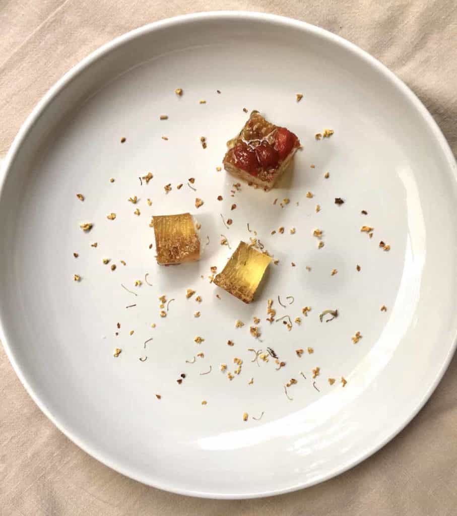 3 square golden osmanthus konnyaku jellies on a plate with flowers scattered around