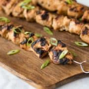 3 grilled chicken skewers on a wooden board.