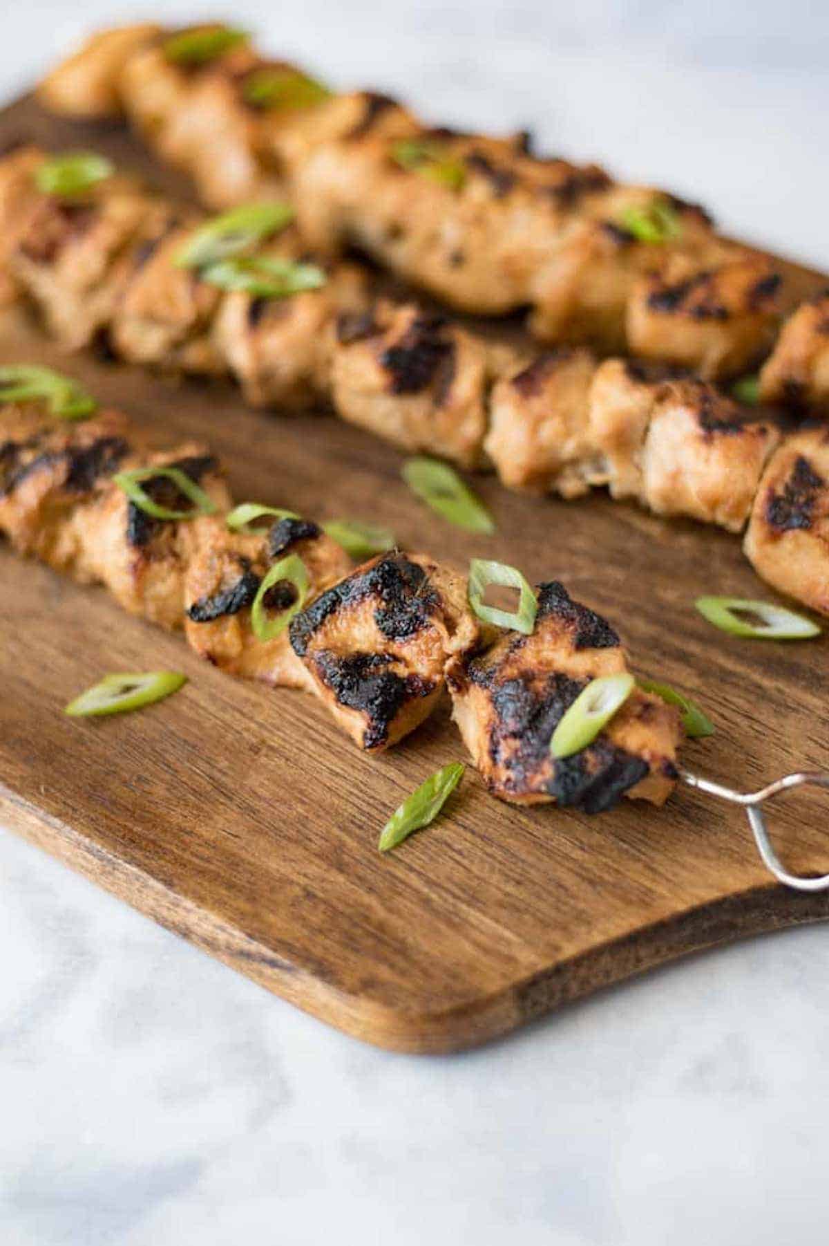 3 grilled chicken skewers on a wooden board.