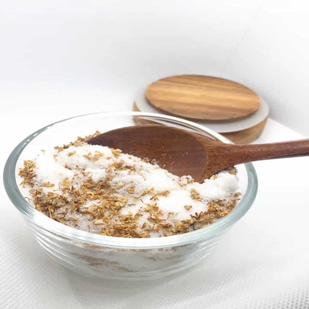 Scooping homemade infused osmanthus sugar out of a glass bowl