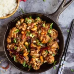 Pieces of cauliflower mixed with dried chilies, cashews and spring onions in a skillet.