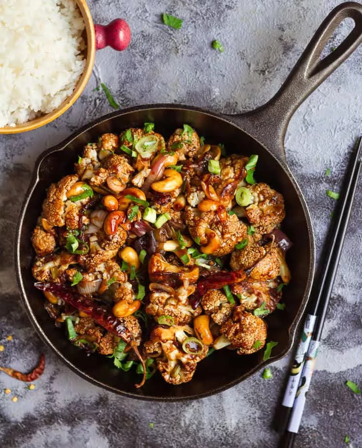 Pieces of cauliflower mixed with dried chilies, cashews and spring onions in a skillet.