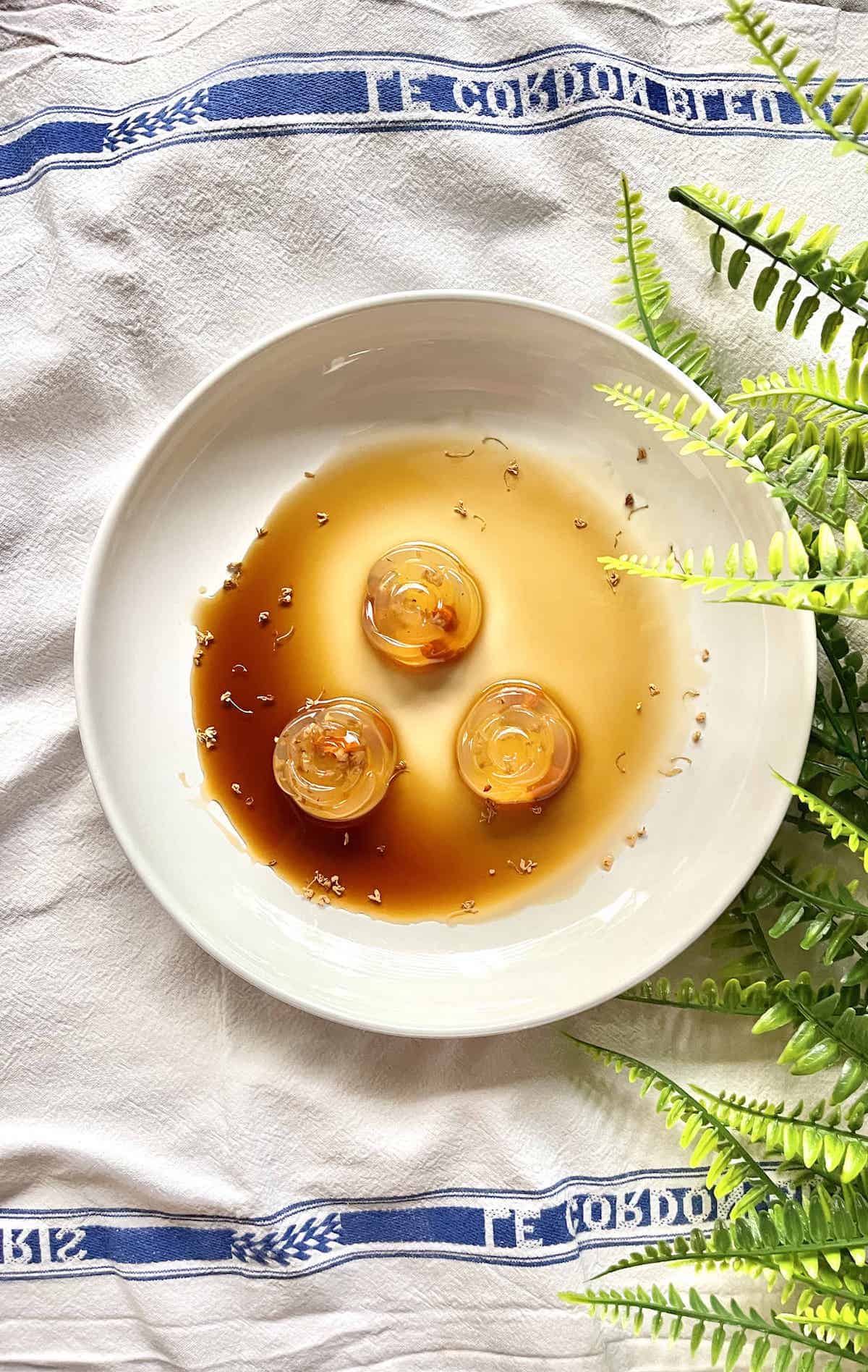 3 osmanthus jellies in brown sugar syrup on a white plate.