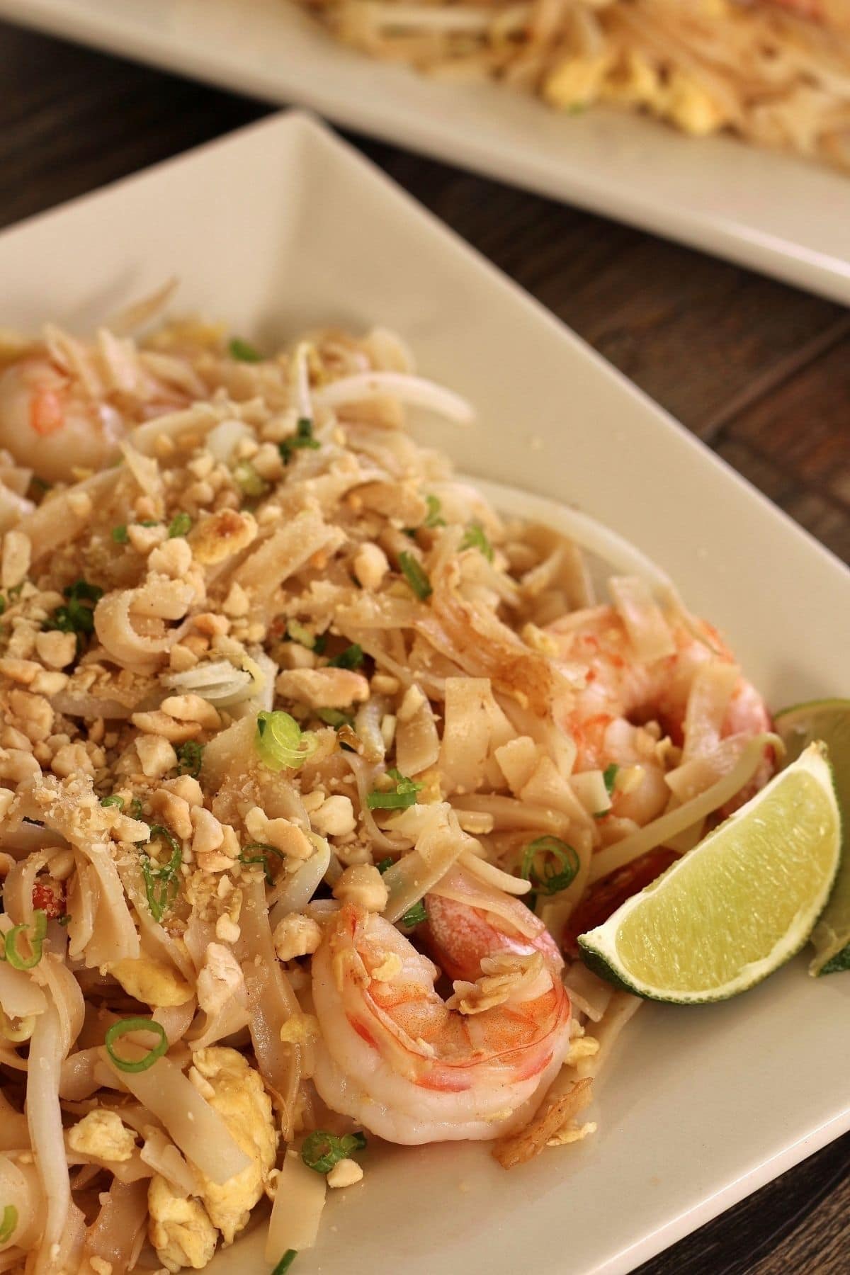 Pad Thai noodles on a white palte with a wedge of lime.