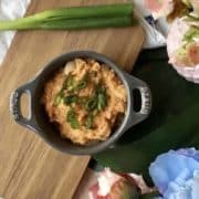 A grey Cocotte filled with a spicy sambal tuna dip and spring onions, placed next to a spring onion and flowers.