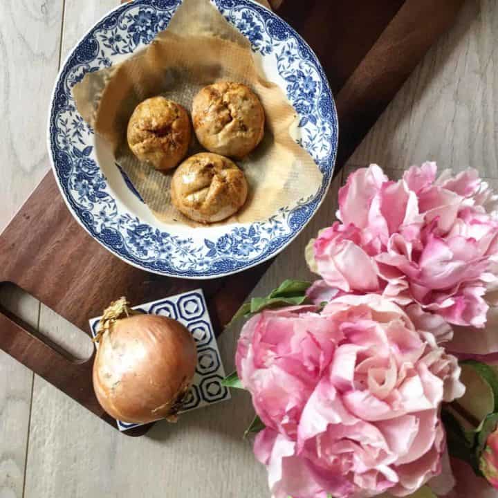 3 bread rolls stuffed with a spicy tuna coconut dip on a blue vintage plate, next to an onion and pink peonies