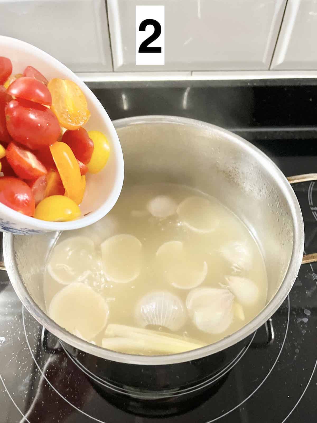 Adding tomatoes to a pot of lemongrass, ginger and shallot soup.