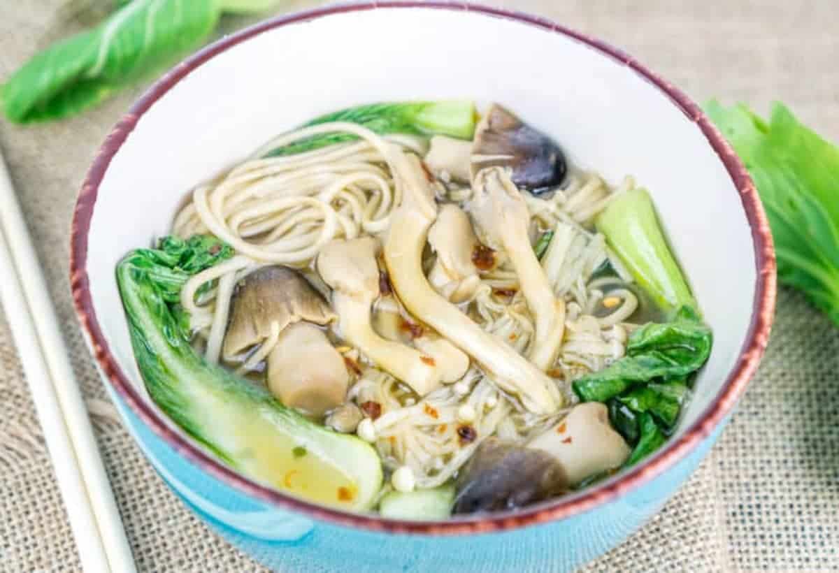 A bowl of noodles with mushrooms and bok choy.
