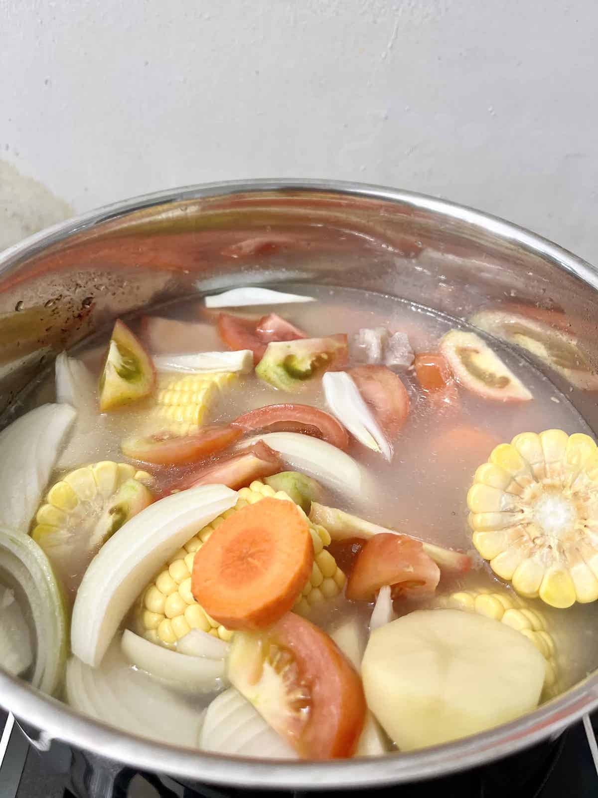 A big pot of carrots, corn, tomatoes, pork and onions simmering on the stove.