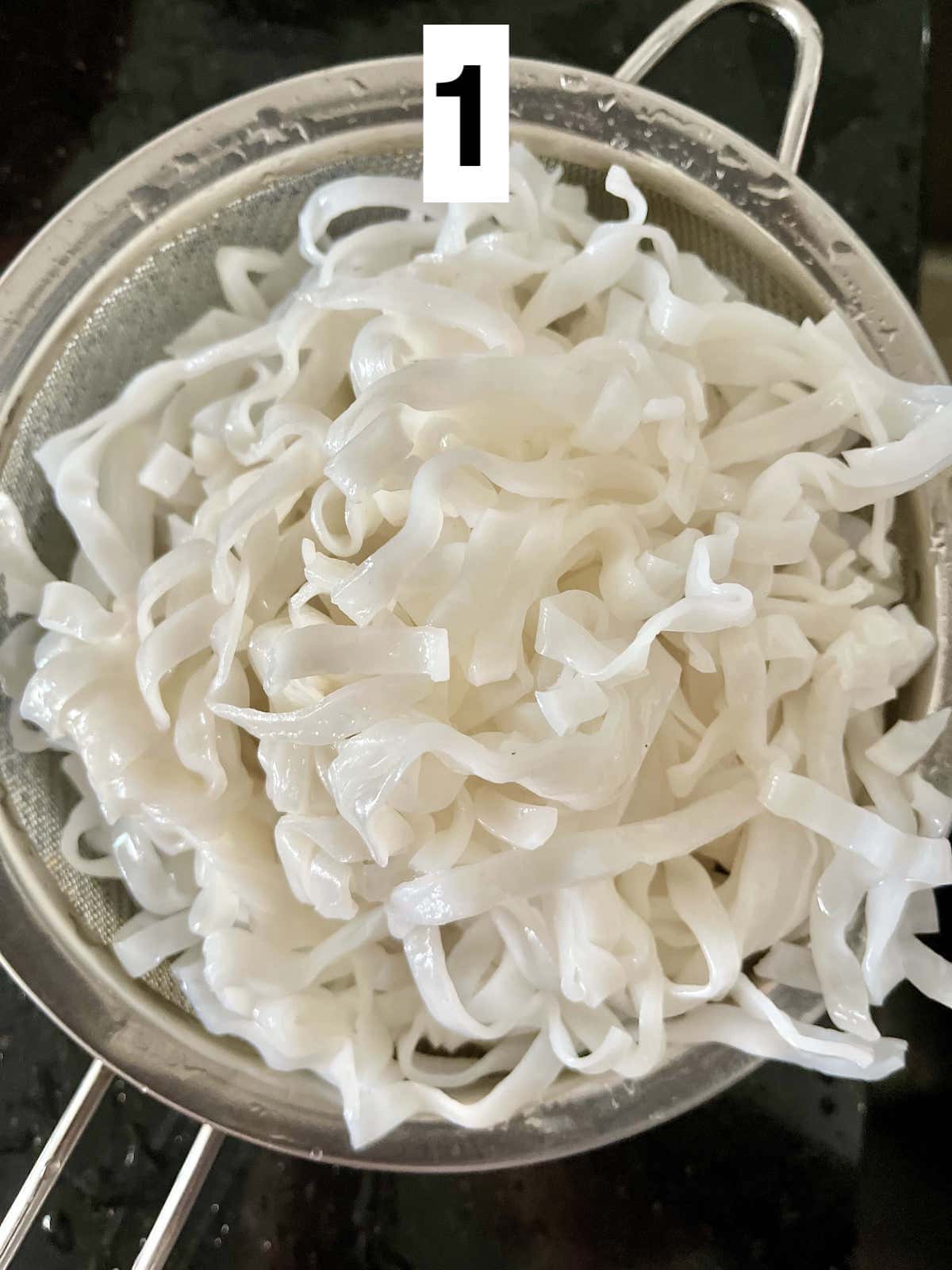 Rinsing fresh rice noodles in a metal sieve.