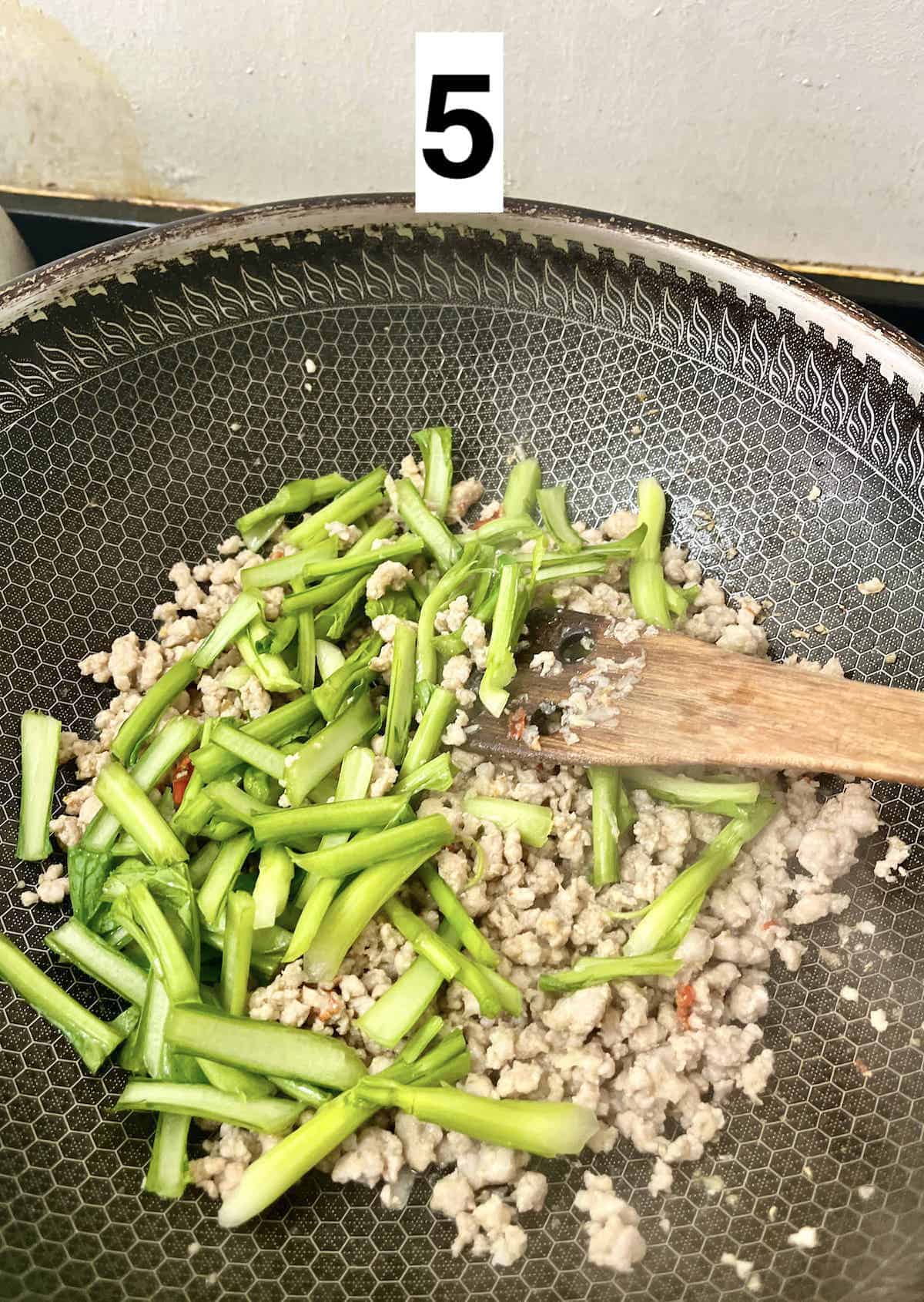 Cut vegetable stems on top of ground pork in a wok.