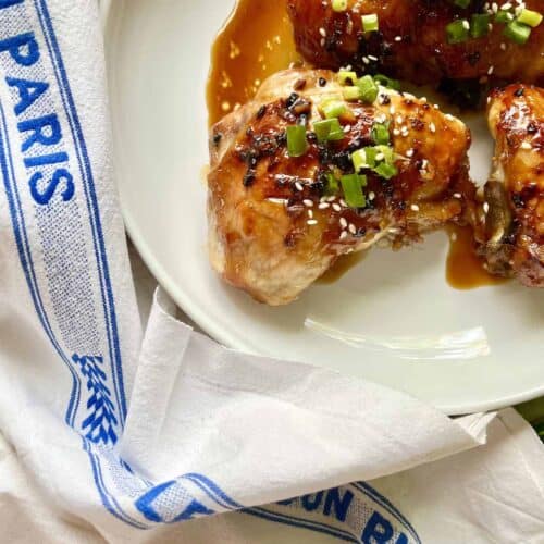 Close-up of 3 baked teriyaki chicken thighs on a white plate.