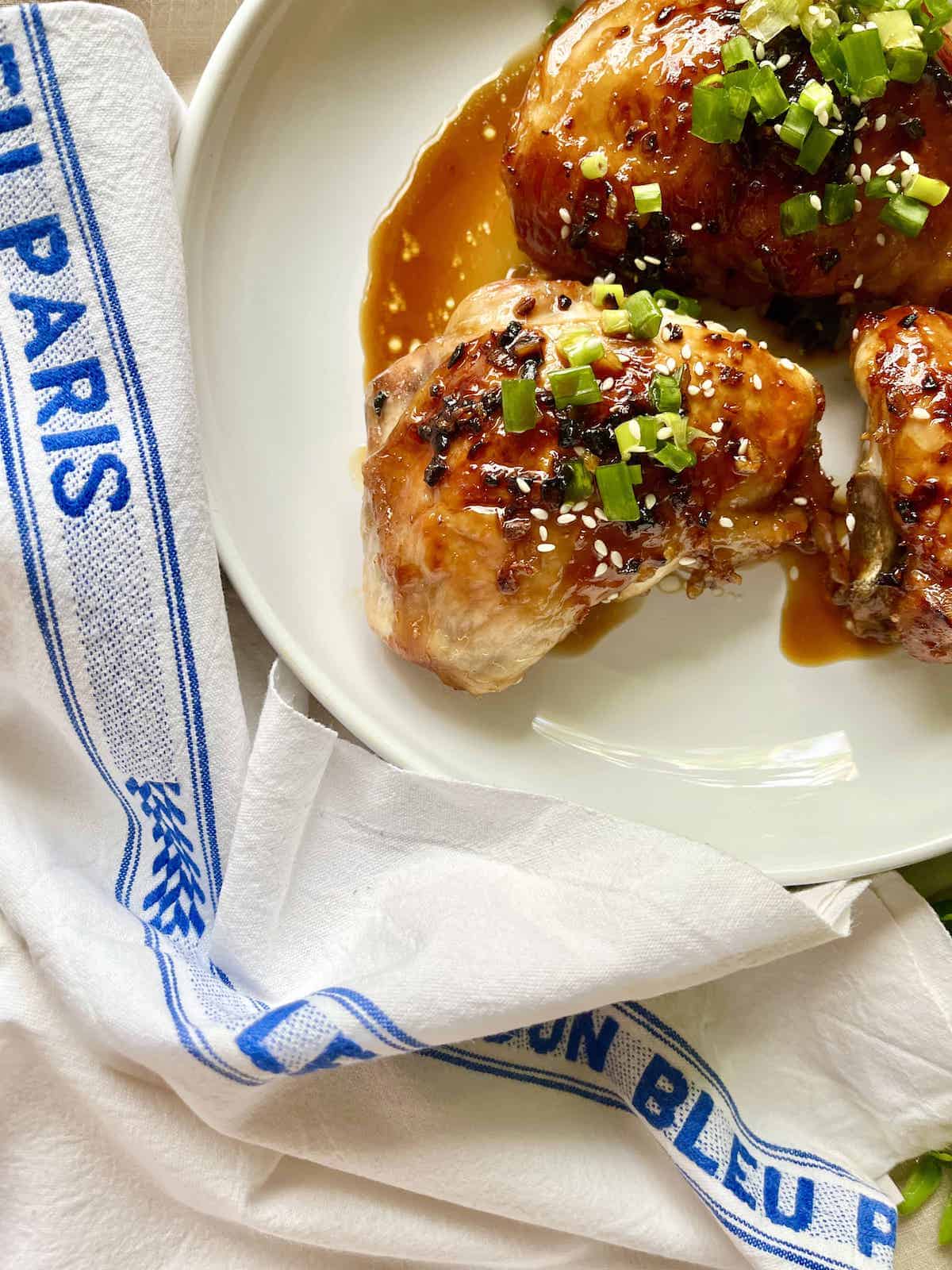 Close-up of 3 baked teriyaki chicken thighs on a white plate.