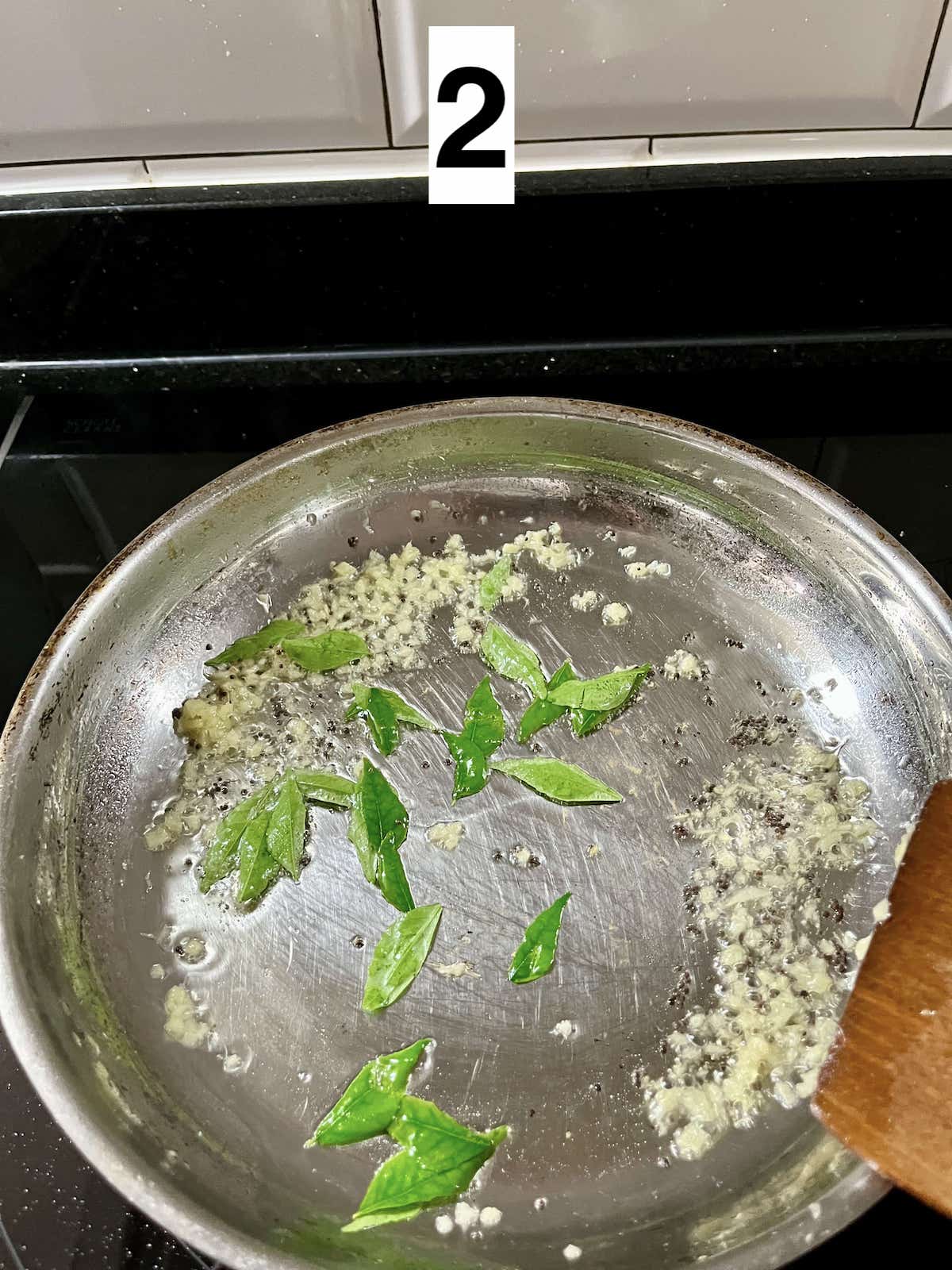 Sauteeing curry leaves, ginger and mustard seeds in a small pan.