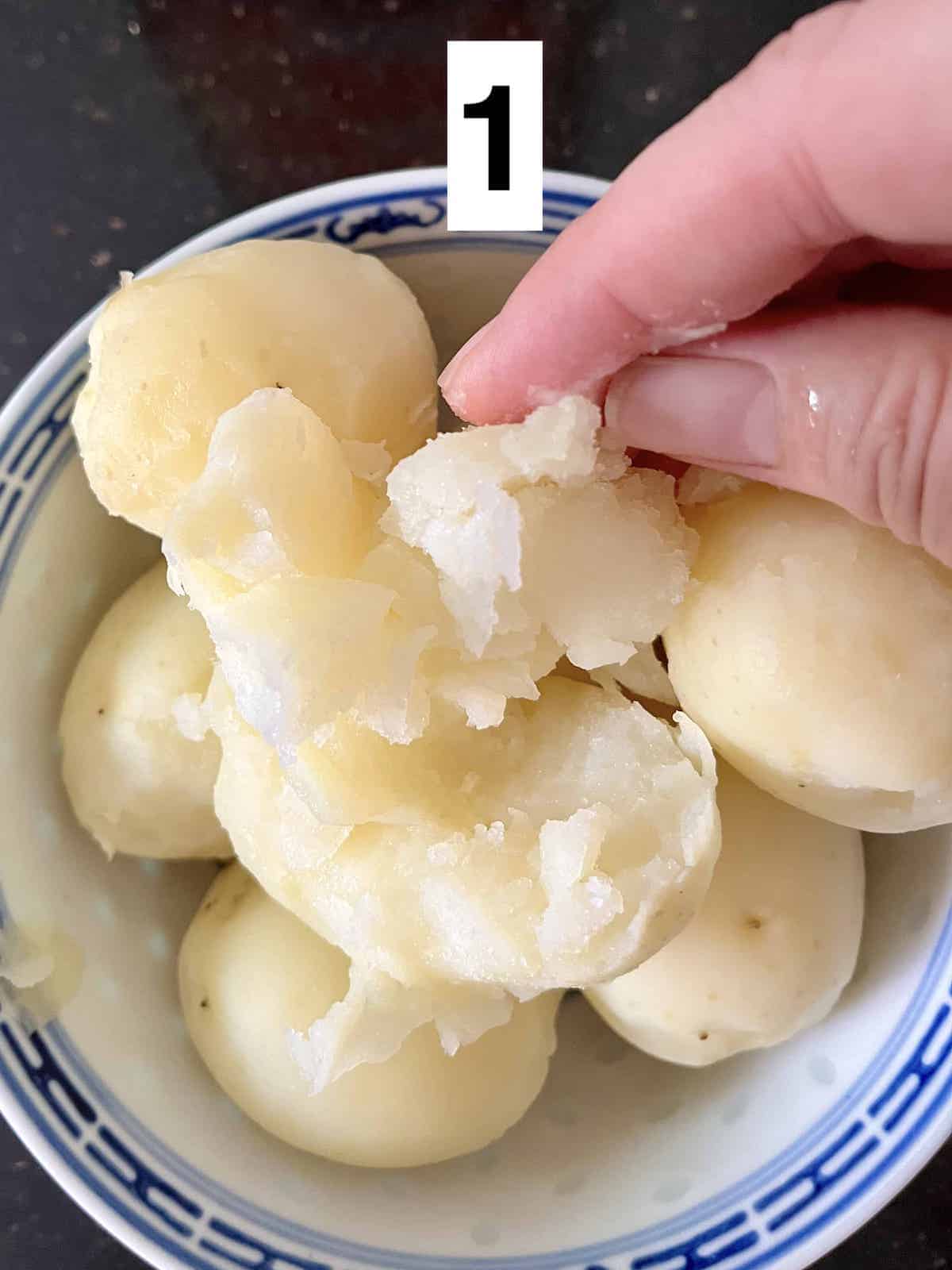 A hand crumbling up boiled potatoes.