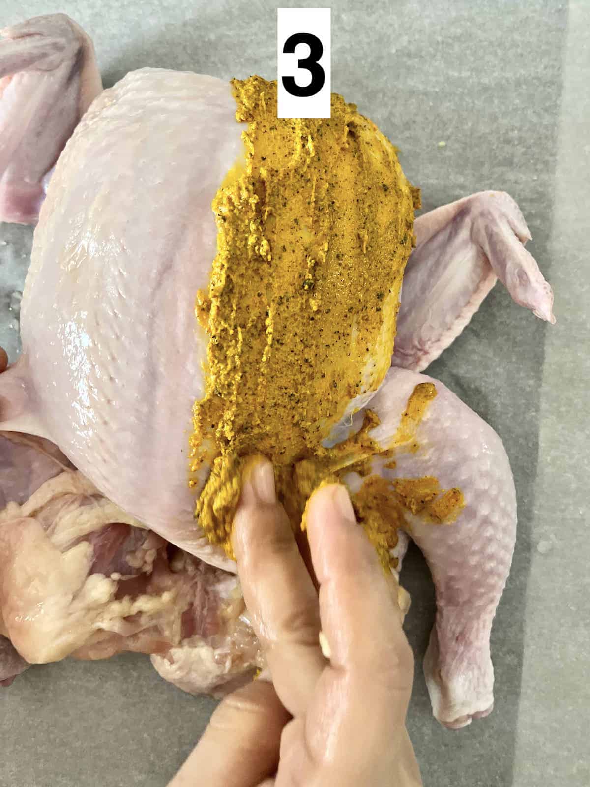 Rubbing turmeric paste all over a whole chicken.