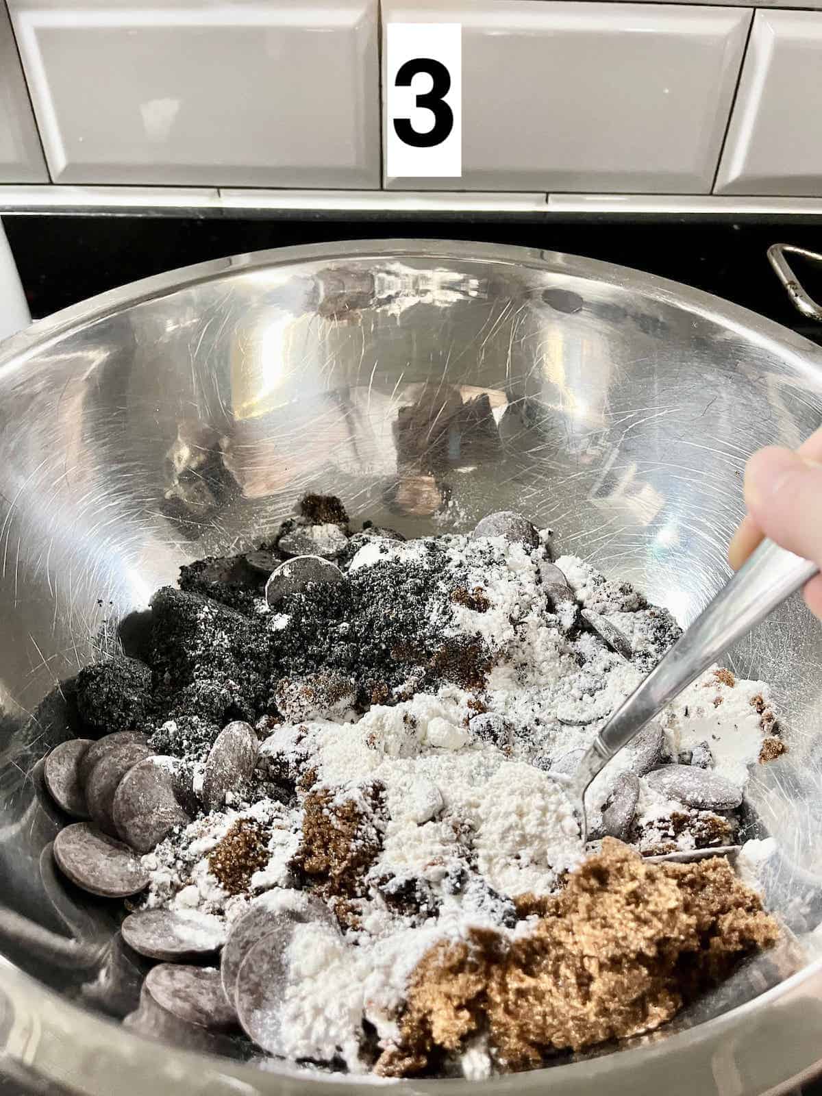 Mixing flour, brown sugar, chocoalte and more in a large silver bowl.