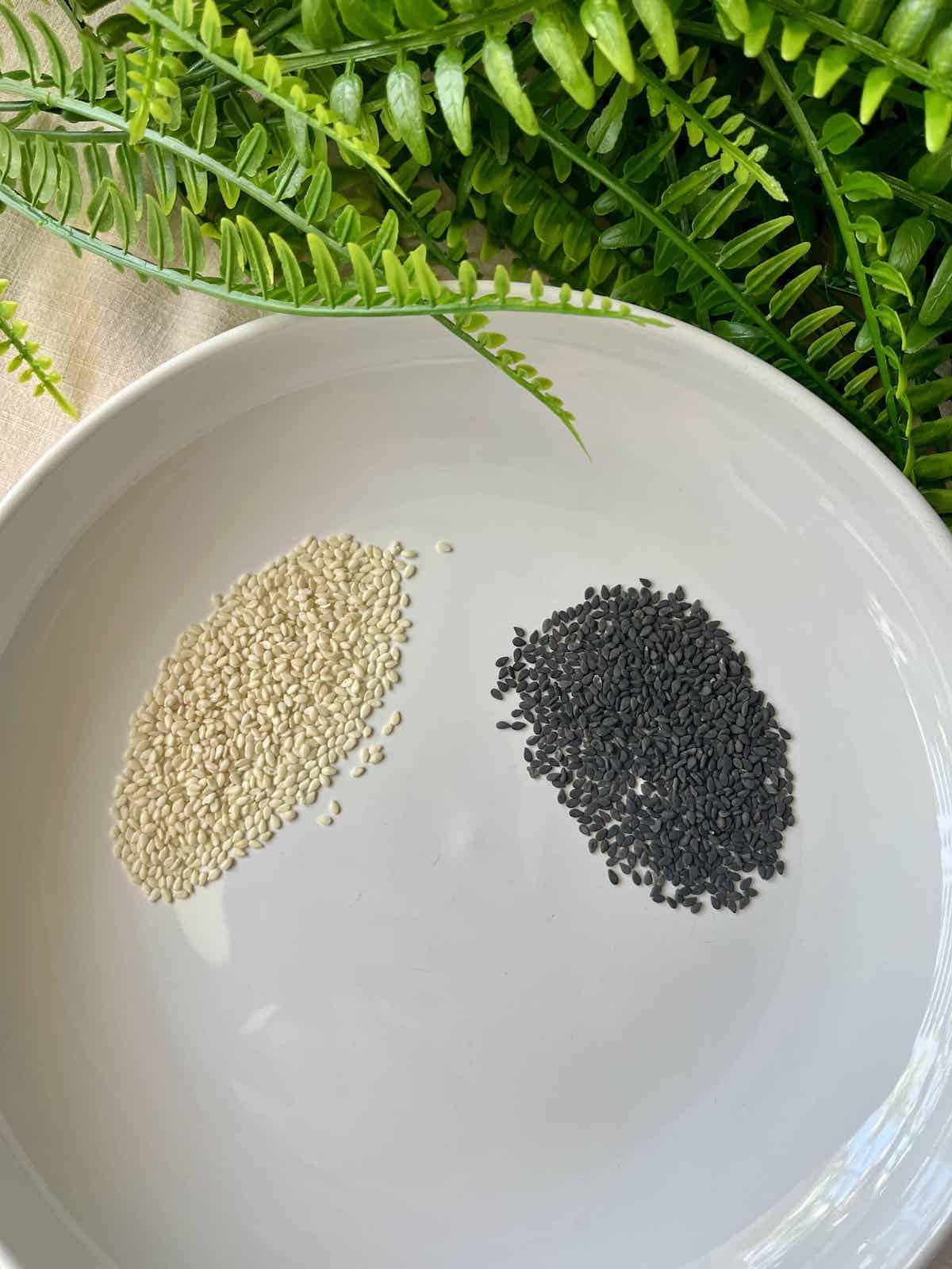 White sesame seeds next to black sesame seeds on a plate.