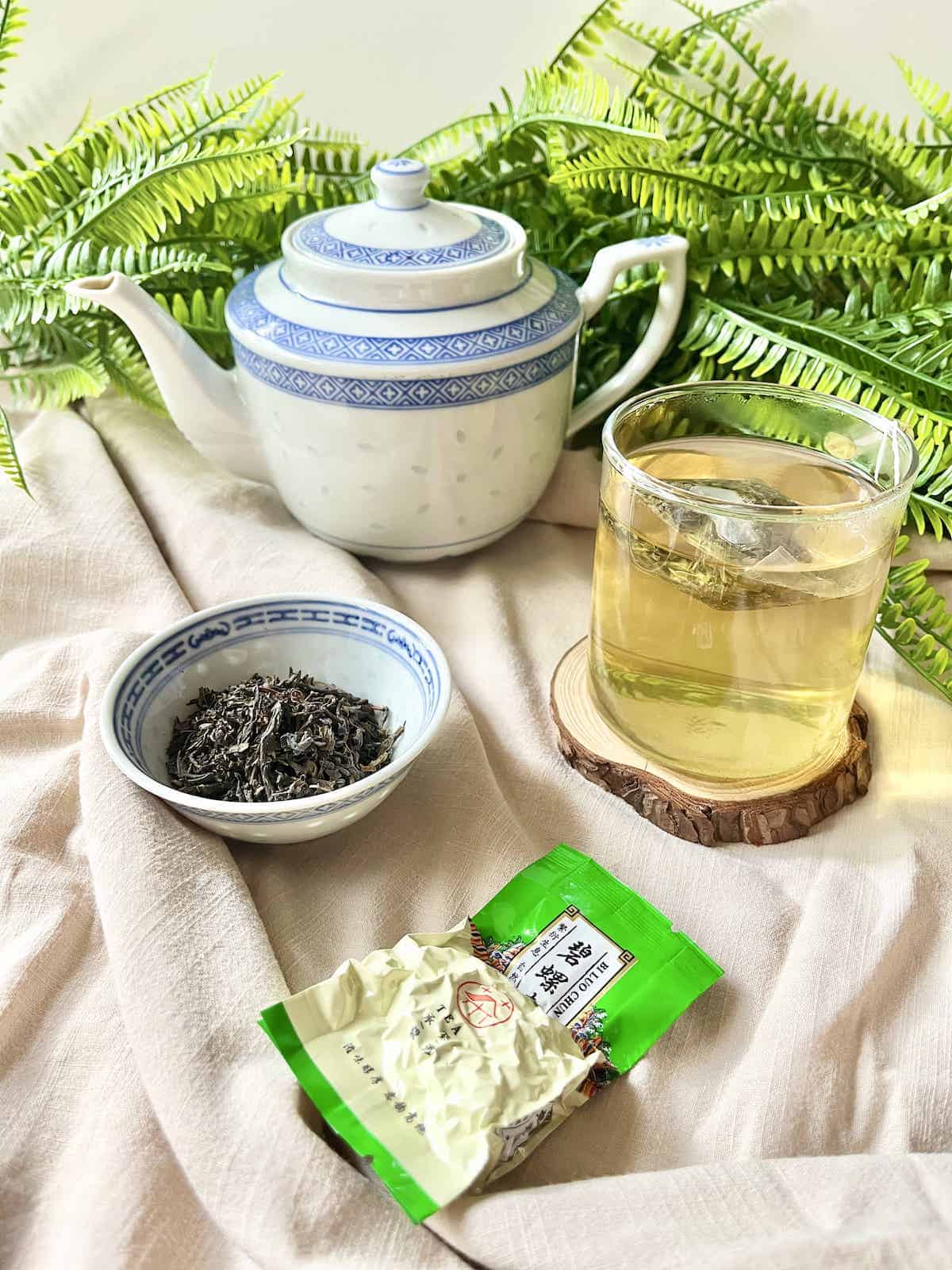 A cup of tea next to tea leaves, a teapot and a sachet of tea.