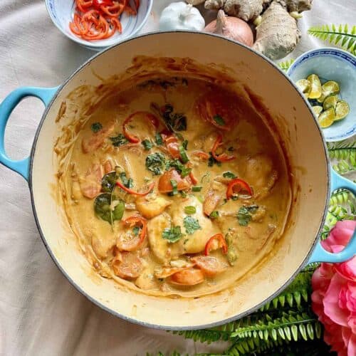 A Dutch oven full of chicken sambal curry, adorned with chili, coriander and kale.