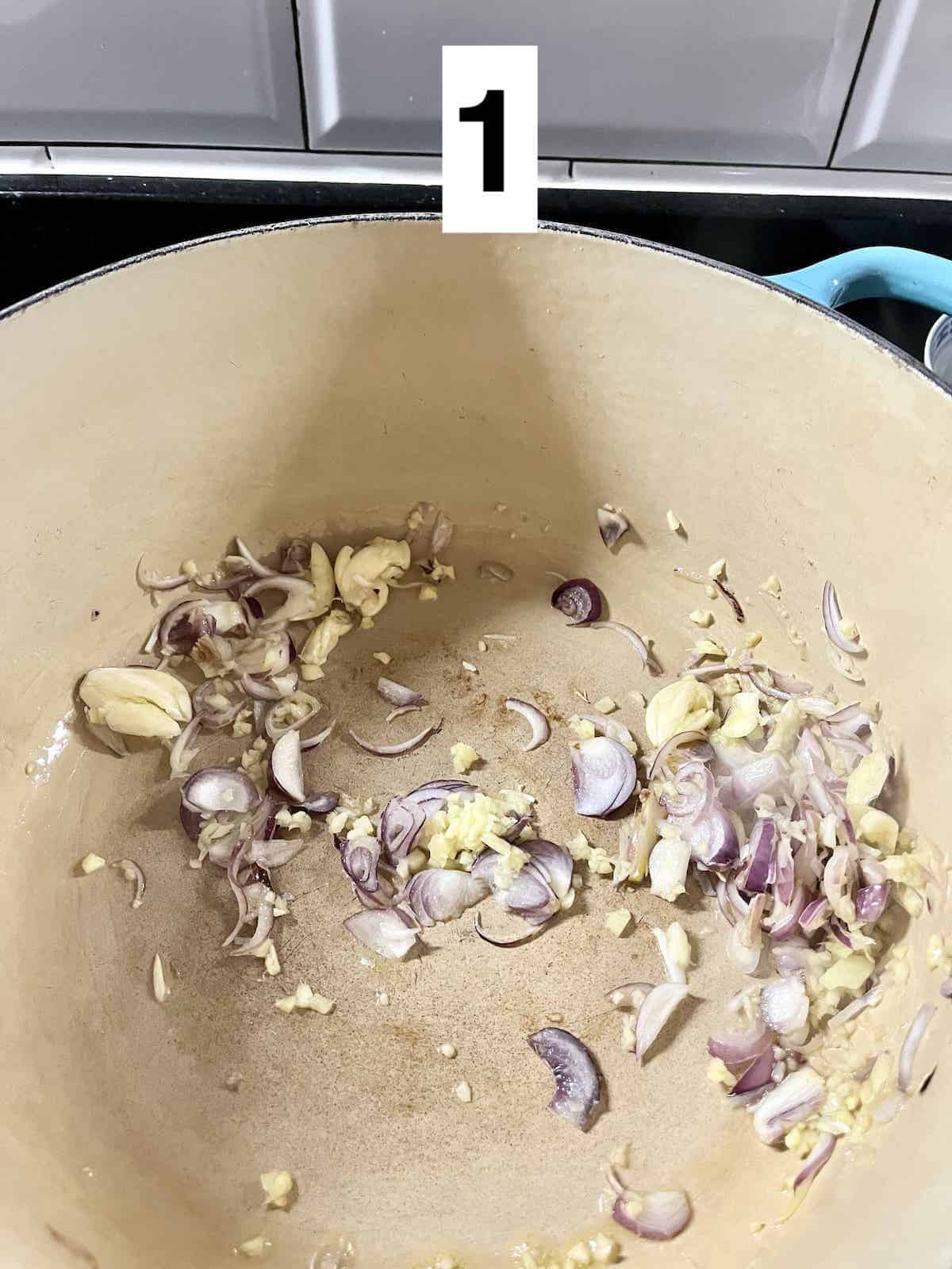 Sliced shallots, gigner and garlic in a Dutch oven.