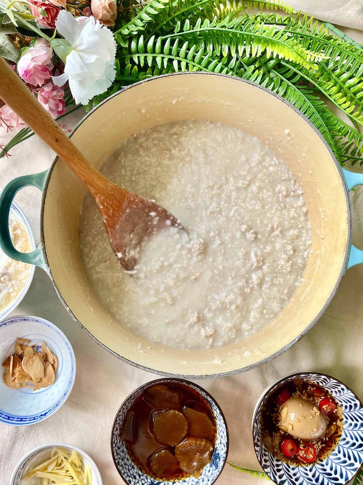 A huge pot of Chinese congee next to soy sauce egg and preserved cucumbers.