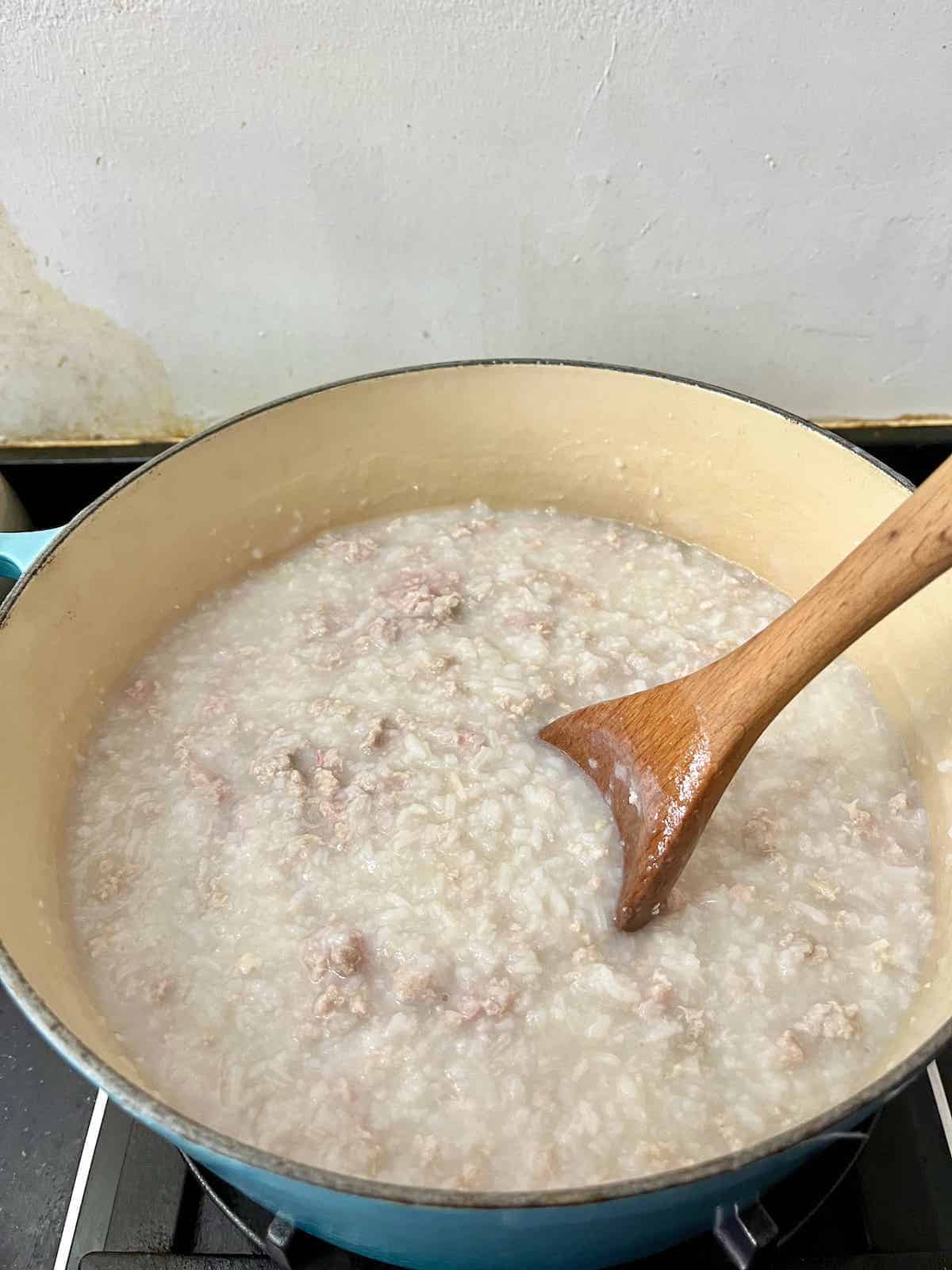 Stirring a pot of pork congee in a Le Creuset Dutch oven.