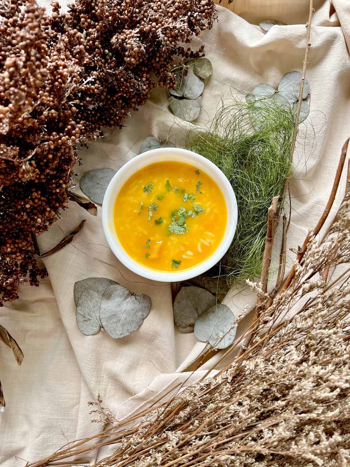 A bowl of warm orange Chinese pumpkin porridge next to fall decor.