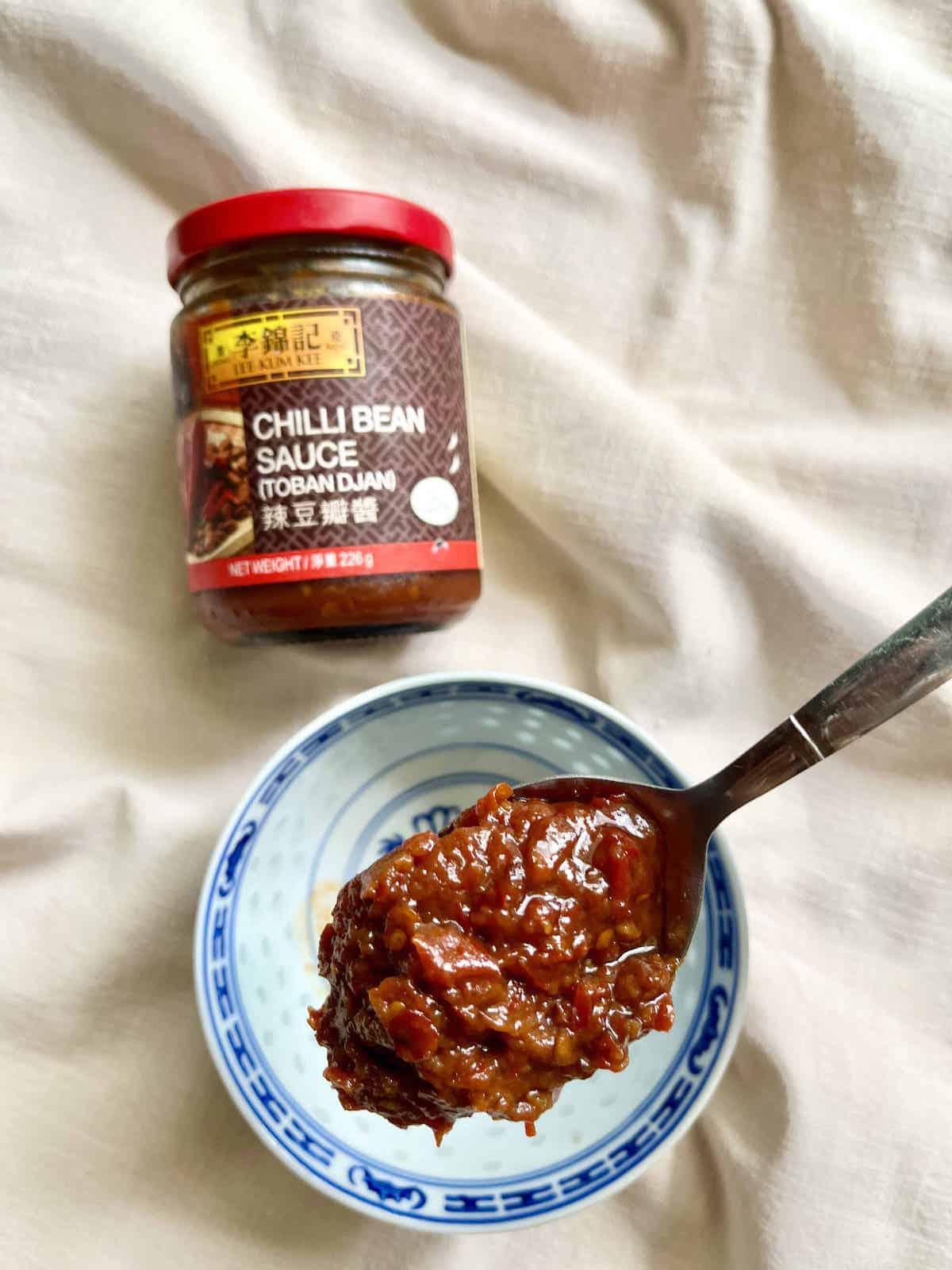 A spoonful of Doubanjiang Sauce with a Lee Kum Kee bottle behind.