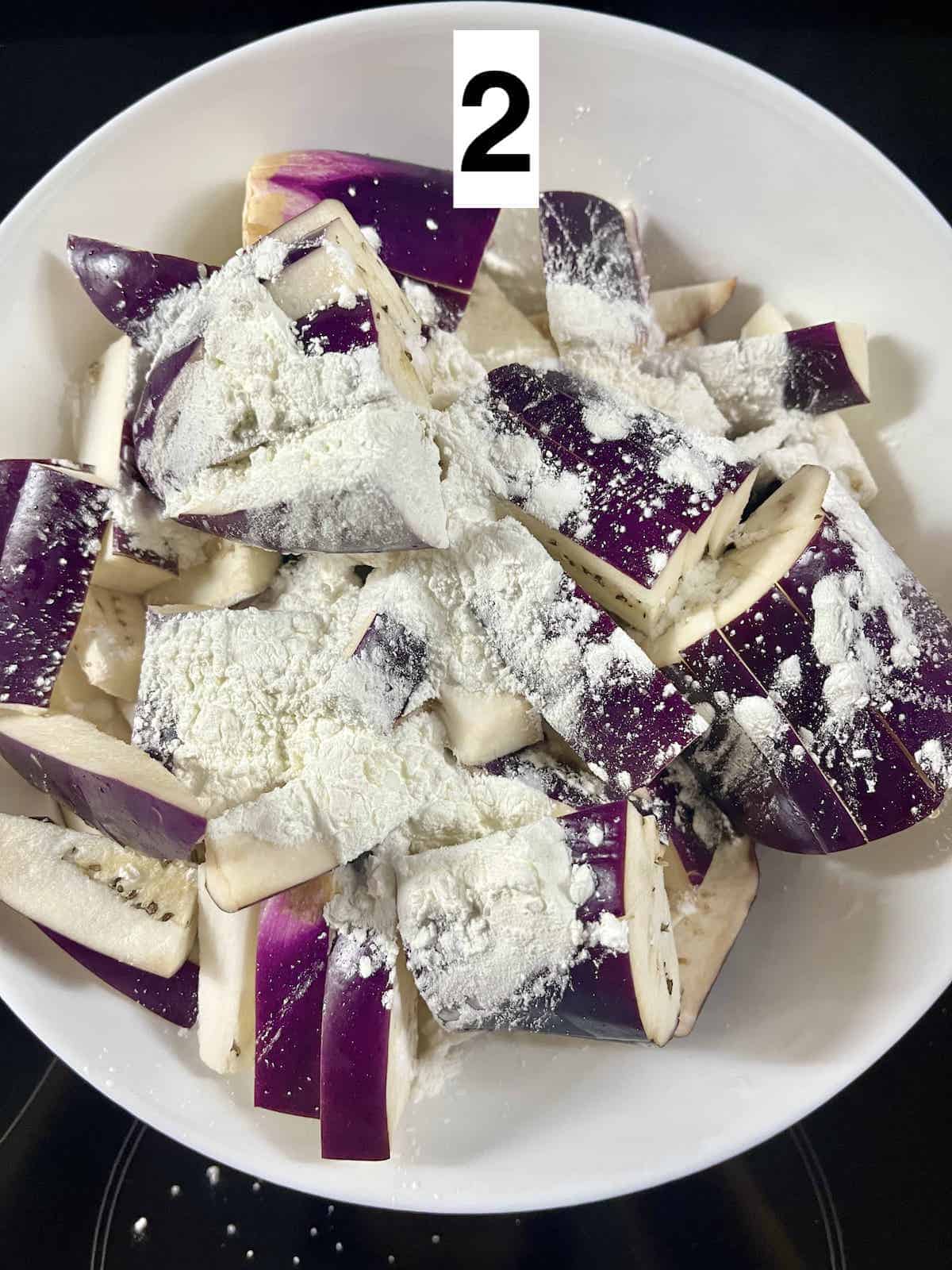 Cornstarch on top of a bowl of cup up eggplants.
