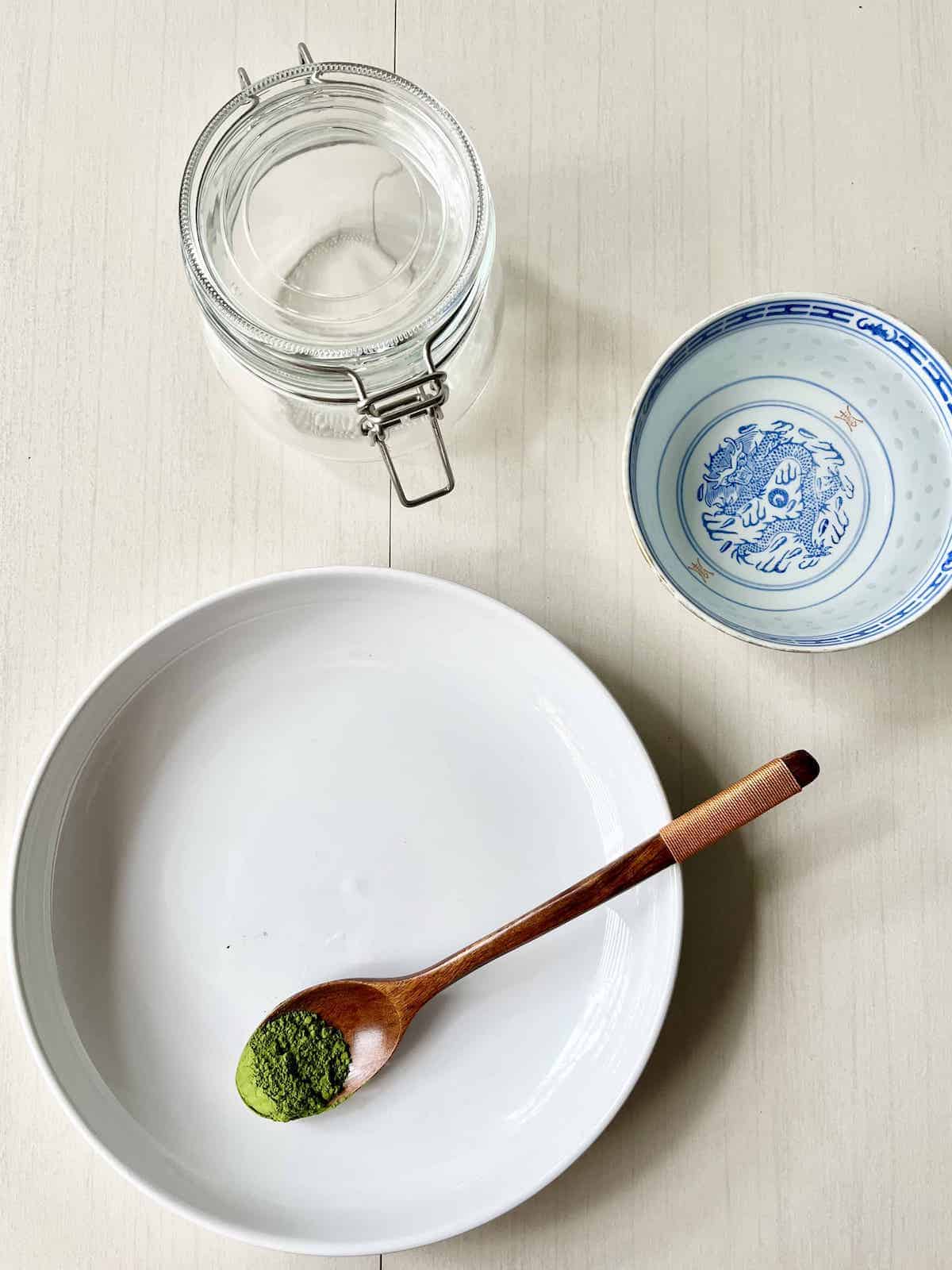 A spoonful of matcha powder next to water and a mason jar.