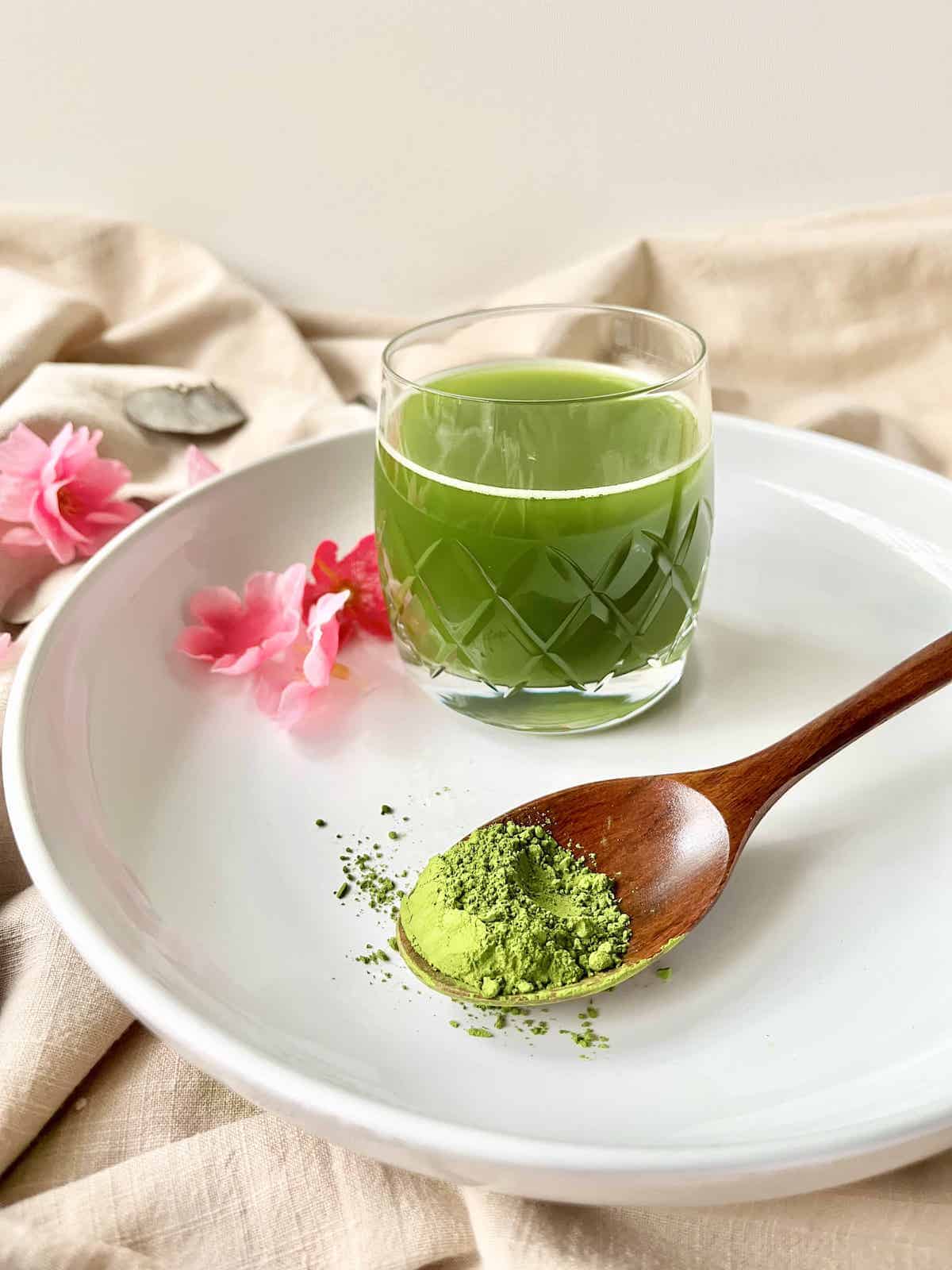 A glass of homemade cold matcha with matcha powder in front of it.