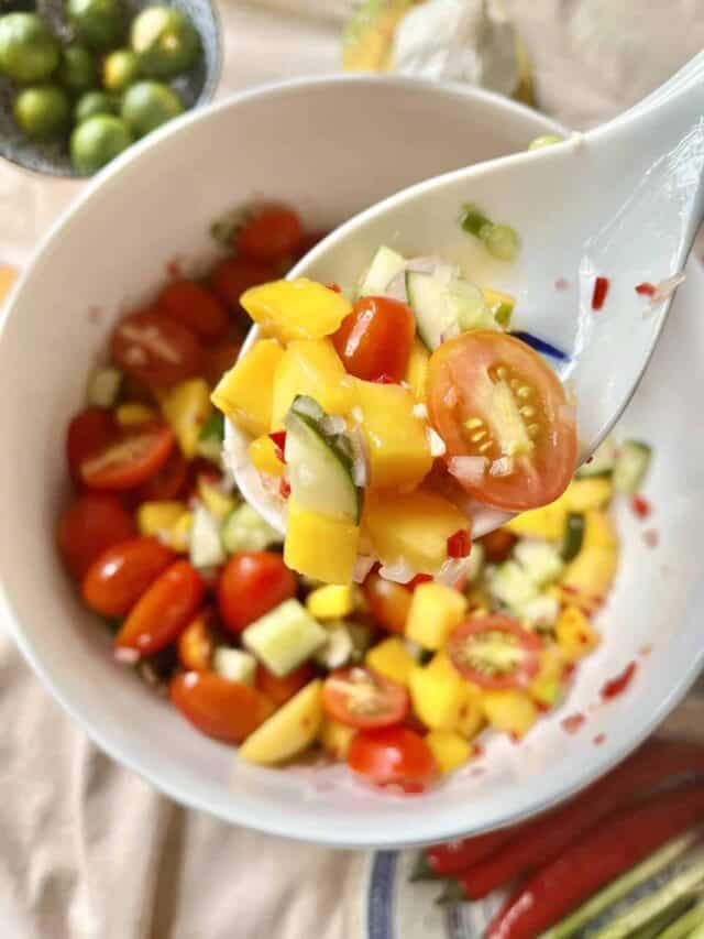 A white spoon holding up a cucumber mango salad mix.