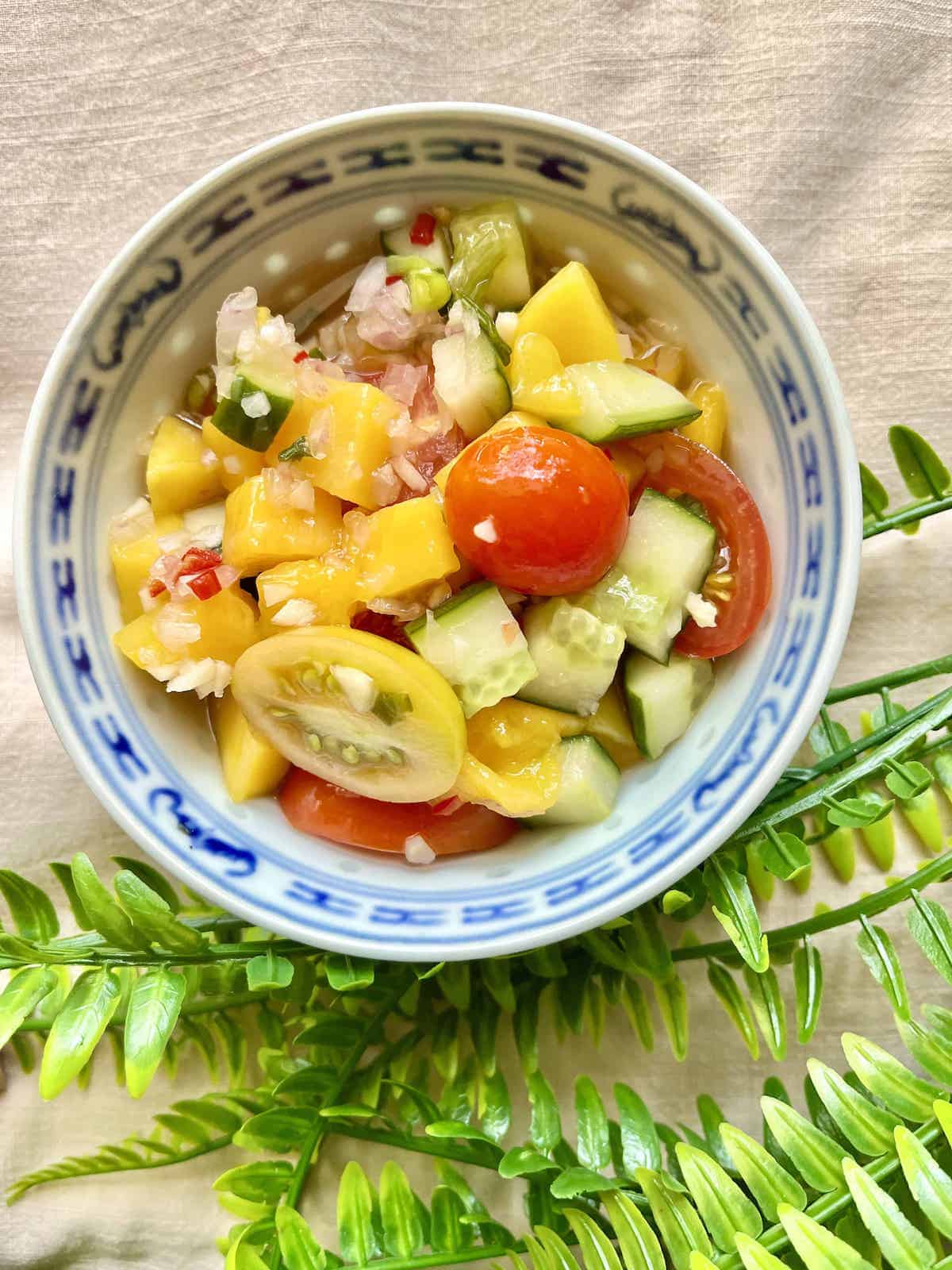 A bowl full of mangoes, tomatoes and cucumber salad.