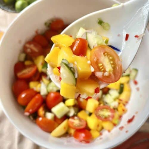 A white spoon holding up a cucumber mango salad mix.