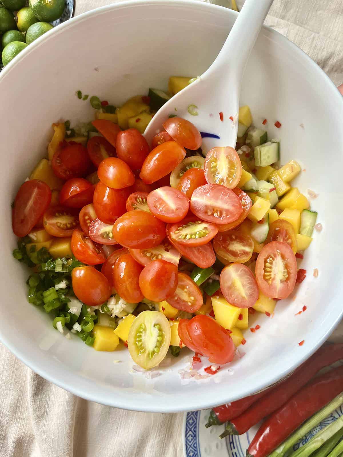 Using a spoon to mix tomato halves, mango cubes and cucumbers.