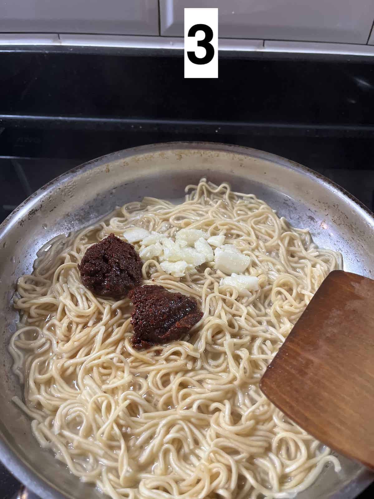 Gochujang sauce and garlic on noodles in a pan.